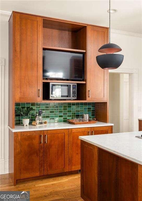629 Hansell St SE, Atlanta, GA 30312 - kitchen featuring stainless steel microwave, light countertops, backsplash, ornamental molding, and brown cabinetry