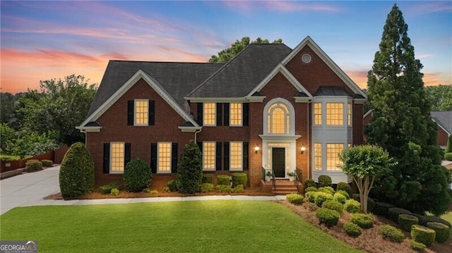 georgian-style home with a yard, brick siding, and concrete driveway