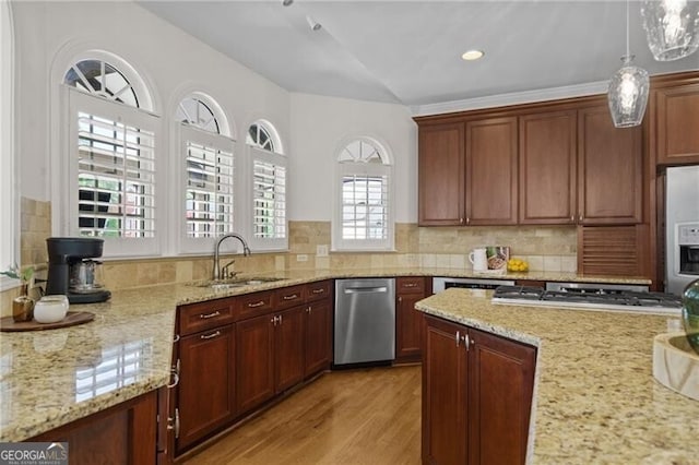 kitchen with a sink, appliances with stainless steel finishes, light wood finished floors, light stone counters, and pendant lighting