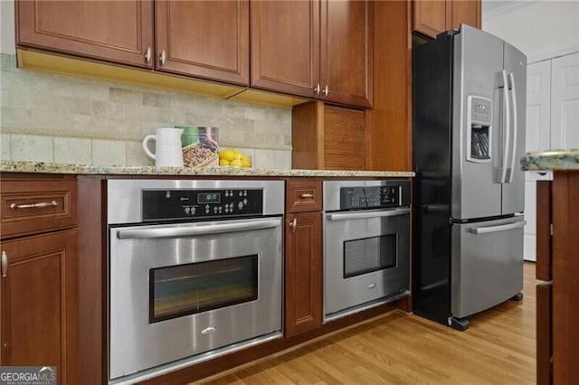 kitchen with stainless steel appliances, light wood-style floors, brown cabinets, light stone counters, and backsplash