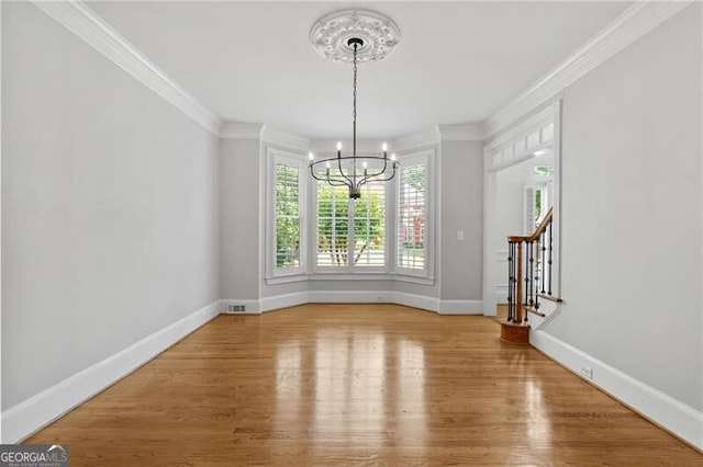 unfurnished dining area with a chandelier, crown molding, wood finished floors, baseboards, and stairway