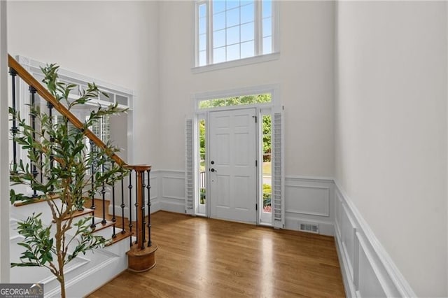 entrance foyer featuring a decorative wall, stairs, a wainscoted wall, a high ceiling, and wood finished floors