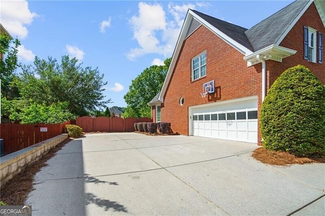 view of side of home with brick siding, driveway, fence, a garage, and a shingled roof