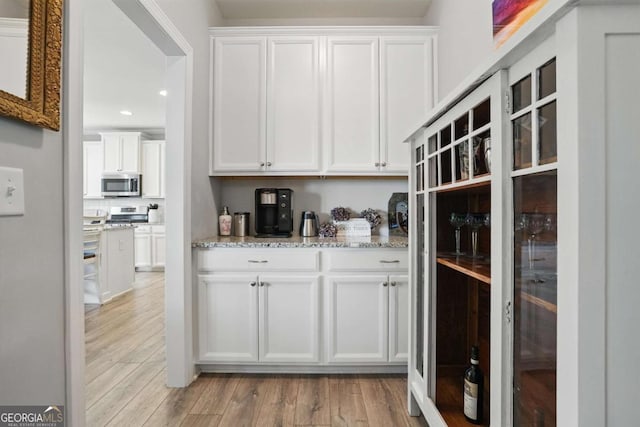 kitchen featuring stainless steel microwave, white cabinetry, light wood finished floors, light stone counters, and recessed lighting
