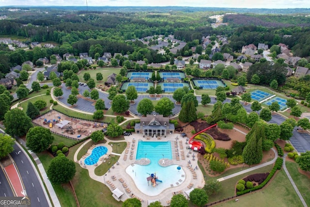 drone / aerial view of a pool area and a heavily wooded area