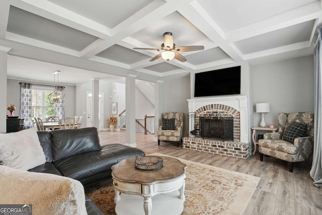 living room with wood finished floors, coffered ceiling, a ceiling fan, a brick fireplace, and beamed ceiling