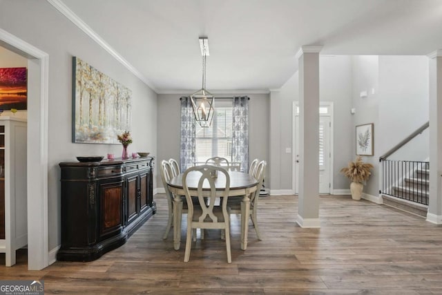 dining room with wood finished floors, decorative columns, crown molding, baseboards, and stairs