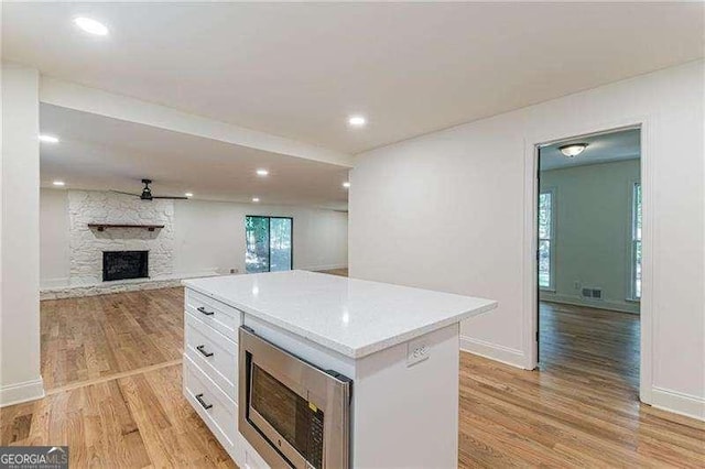 418 Mockingbird Ln, Smyrna, GA 30082 - kitchen with stainless steel microwave, white cabinetry, light wood-style floors, a stone fireplace, and a kitchen island