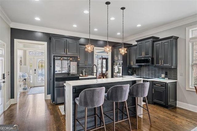 1525 Camden Cove Dr, Cumming, GA 30040 - kitchen with stainless steel microwave, a kitchen island with sink, tasteful backsplash, light countertops, and crown molding