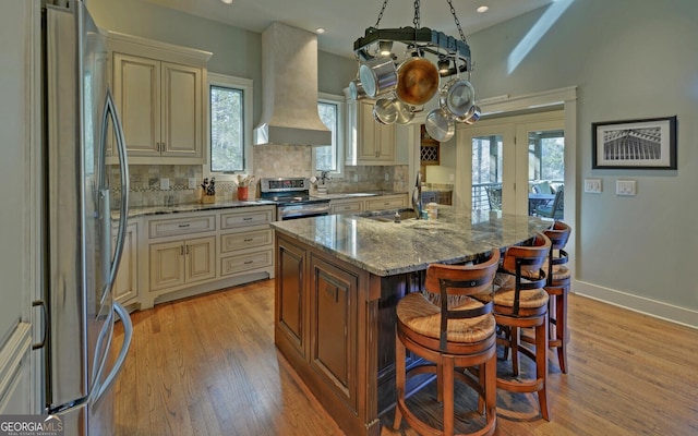 kitchen featuring cream cabinetry, stainless steel appliances, premium range hood, a sink, and light wood finished floors