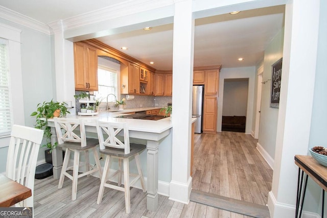 kitchen featuring light countertops, a kitchen breakfast bar, tasteful backsplash, a sink, and light wood-style floors
