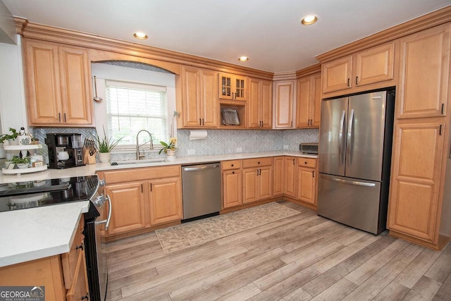 kitchen with stainless steel appliances, a sink, light wood-type flooring, light countertops, and tasteful backsplash