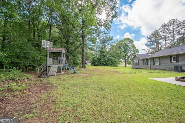 view of grassy yard featuring a playground, cooling unit, and an outdoor fire pit