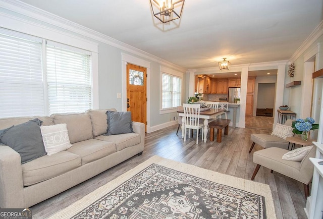living area with a chandelier, light wood-style flooring, crown molding, and baseboards