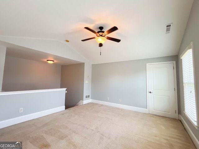 empty room with vaulted ceiling, ceiling fan, baseboards, and light colored carpet