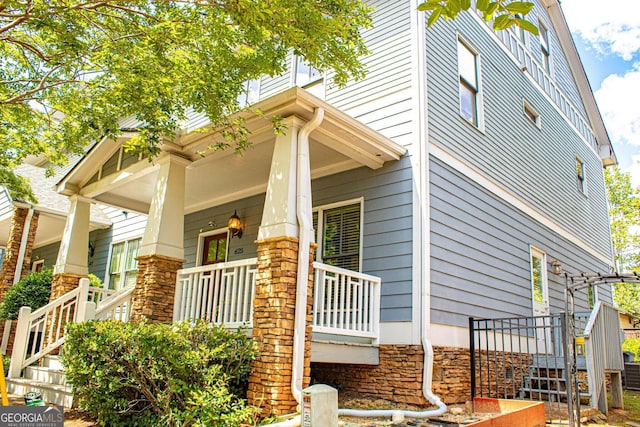 view of property exterior featuring a porch, stone siding, and stairway