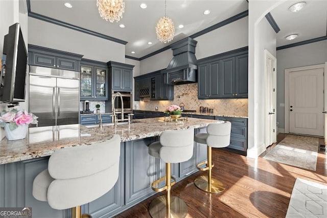 kitchen with built in refrigerator, custom exhaust hood, ornamental molding, a peninsula, and dark wood-style floors