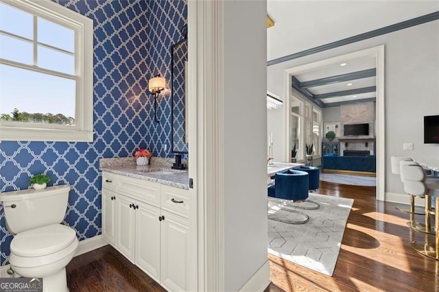 bathroom featuring wallpapered walls, wood finished floors, toilet, baseboards, and vanity