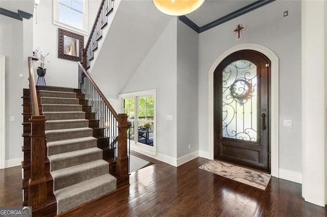 foyer entrance with wood finished floors, arched walkways, baseboards, stairs, and a towering ceiling