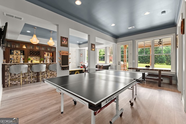 game room featuring ornamental molding, recessed lighting, plenty of natural light, a bar, and wood finished floors