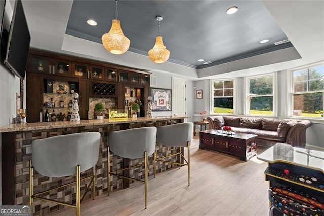 indoor bar with a raised ceiling, light wood-type flooring, crown molding, recessed lighting, and hanging light fixtures