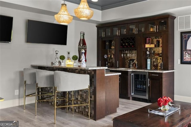 indoor bar with beverage cooler, light wood-style flooring, hanging light fixtures, and baseboards