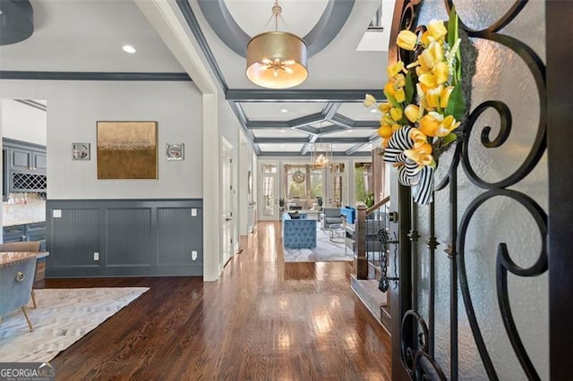 foyer featuring coffered ceiling, ornamental molding, wood finished floors, wainscoting, and beamed ceiling
