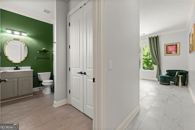 corridor with baseboards, crown molding, light marble finish flooring, and a sink