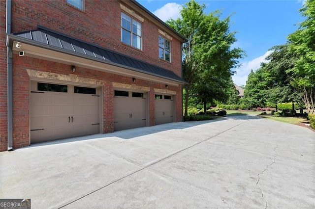 view of side of property featuring a garage, brick siding, a standing seam roof, driveway, and metal roof