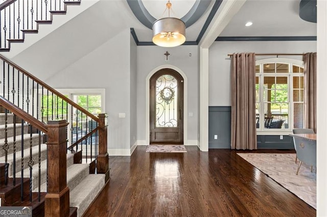 foyer entrance featuring wood finished floors, crown molding, stairway, arched walkways, and baseboards