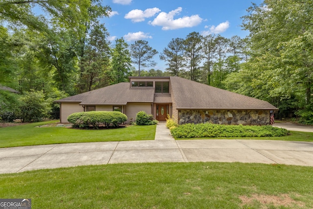 mid-century modern home featuring a front yard, stone siding, and a shingled roof