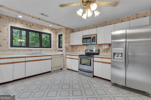 kitchen featuring appliances with stainless steel finishes, wallpapered walls, a sink, light floors, and light countertops