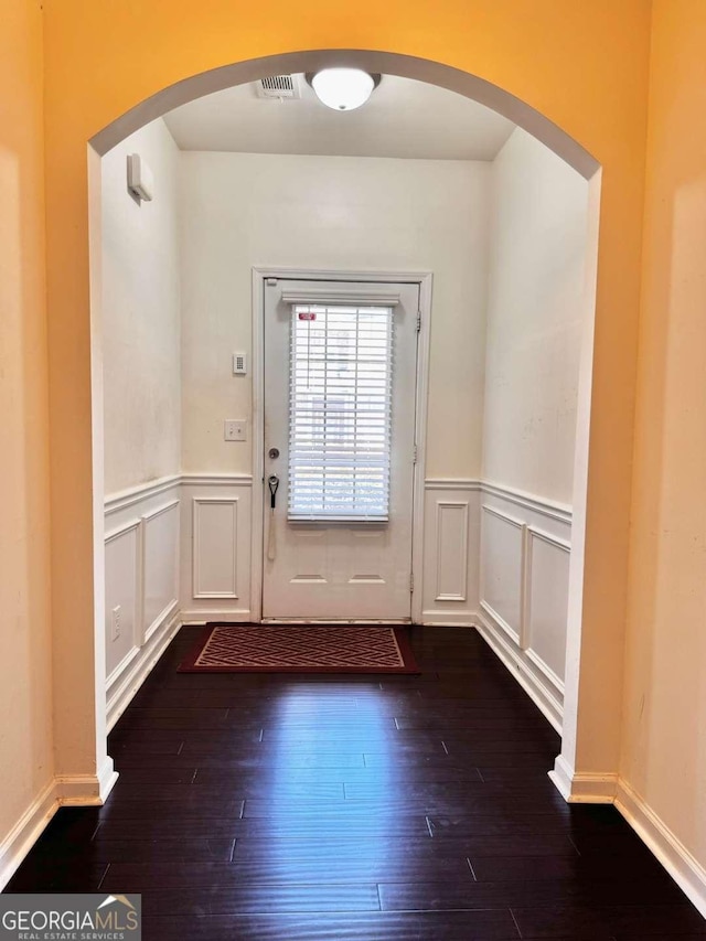 entryway with a wainscoted wall, dark wood finished floors, arched walkways, and a decorative wall