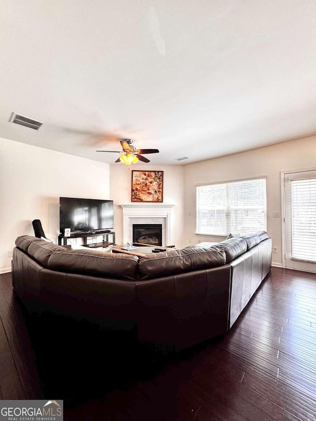 living area with dark wood-style floors, healthy amount of natural light, a ceiling fan, and a fireplace