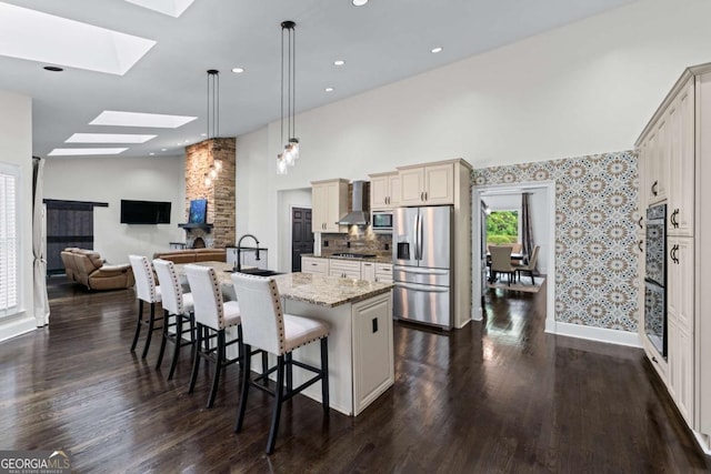 kitchen with stainless steel appliances, a skylight, wall chimney range hood, a breakfast bar, and dark wood-style flooring