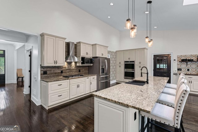 kitchen featuring appliances with stainless steel finishes, wall chimney range hood, a sink, tasteful backsplash, and dark wood-style flooring