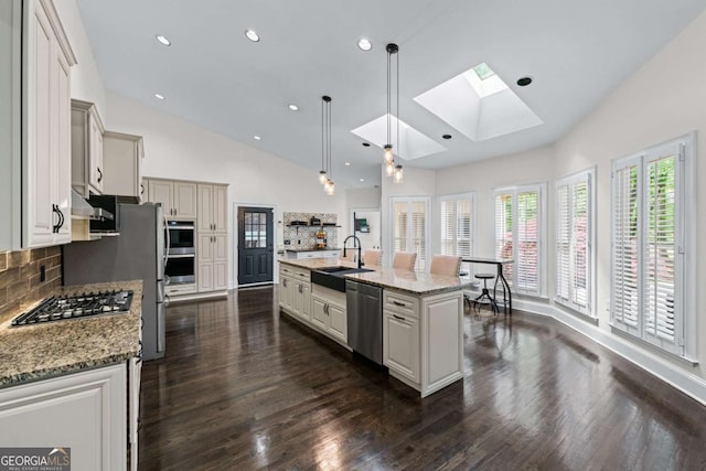 kitchen featuring a sink, a skylight, appliances with stainless steel finishes, tasteful backsplash, and dark wood finished floors