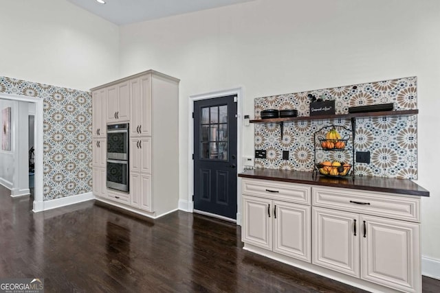 kitchen with double oven, dark wood-type flooring, dark countertops, and baseboards