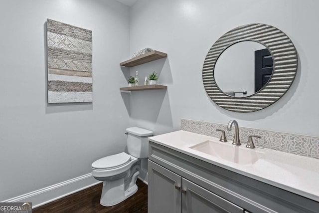 half bath featuring wood finished floors, toilet, baseboards, and vanity