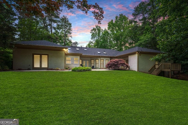 back of house at dusk featuring french doors, stucco siding, a yard, and a chimney