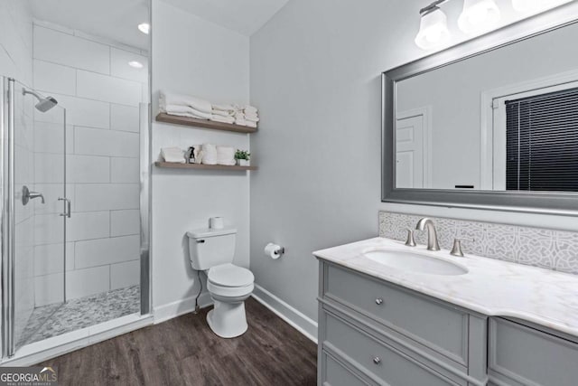 bathroom with toilet, a stall shower, wood finished floors, baseboards, and vanity
