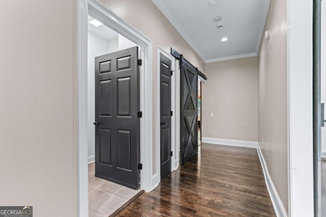 hall featuring a barn door, crown molding, wood finished floors, and baseboards