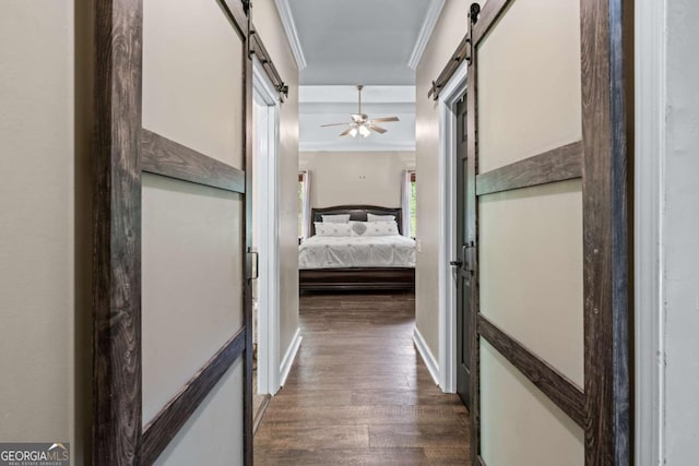corridor with a barn door, ornamental molding, and dark wood-style flooring