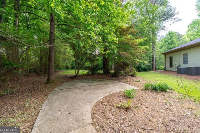 view of yard with central air condition unit, a view of trees, and a patio area