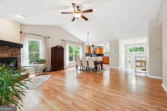 living area with a ceiling fan, light wood-style flooring, healthy amount of natural light, a fireplace, and vaulted ceiling