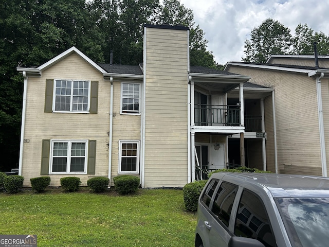 view of side of home featuring a chimney, a balcony, a yard, and brick siding