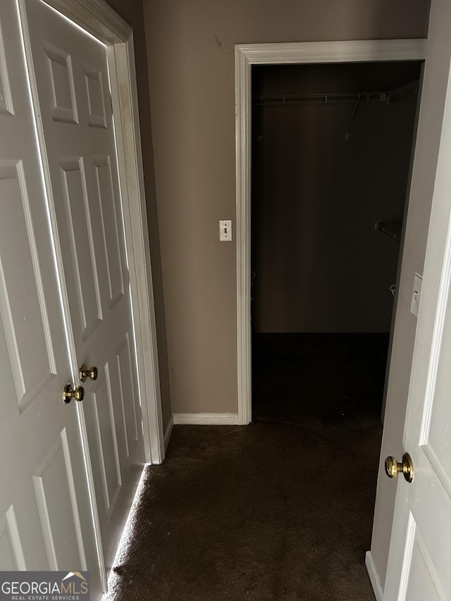 hall featuring dark carpet and baseboards