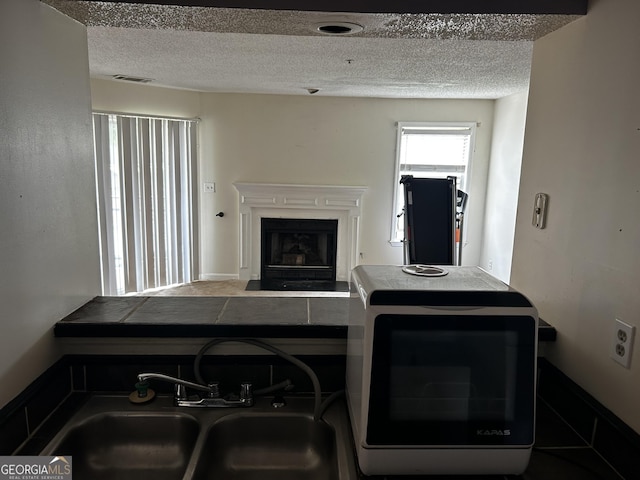 kitchen featuring a sink, a textured ceiling, and a fireplace with flush hearth