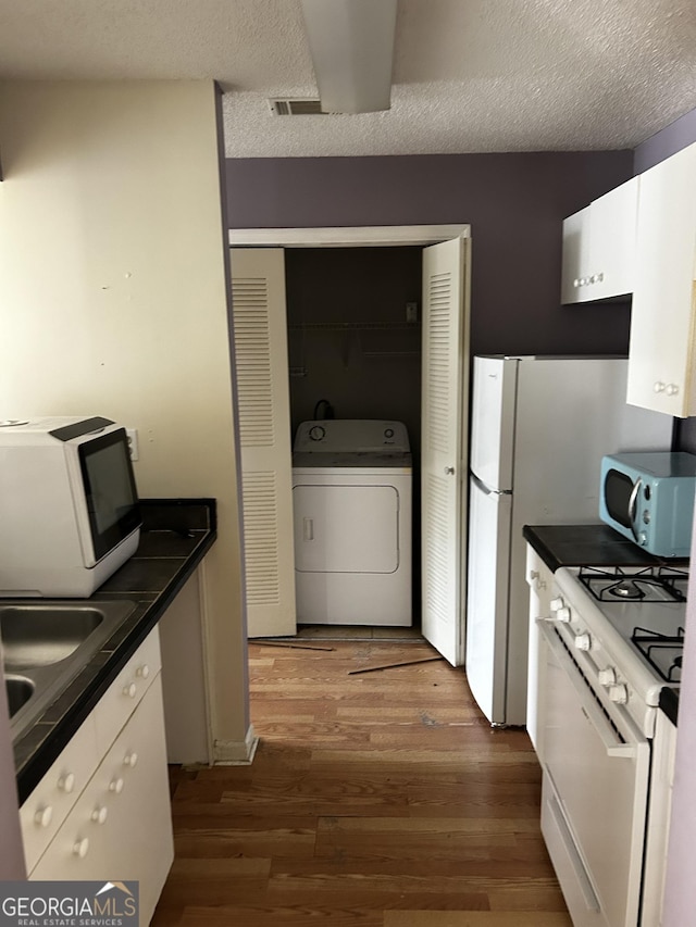 kitchen featuring washer / dryer, white appliances, dark wood-style flooring, dark countertops, and white cabinets