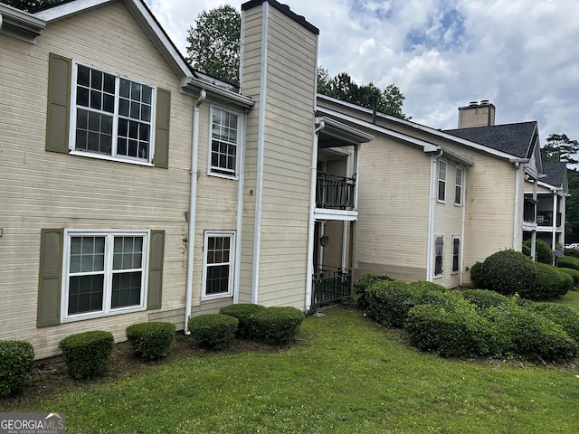 back of property featuring a chimney, a balcony, and a yard